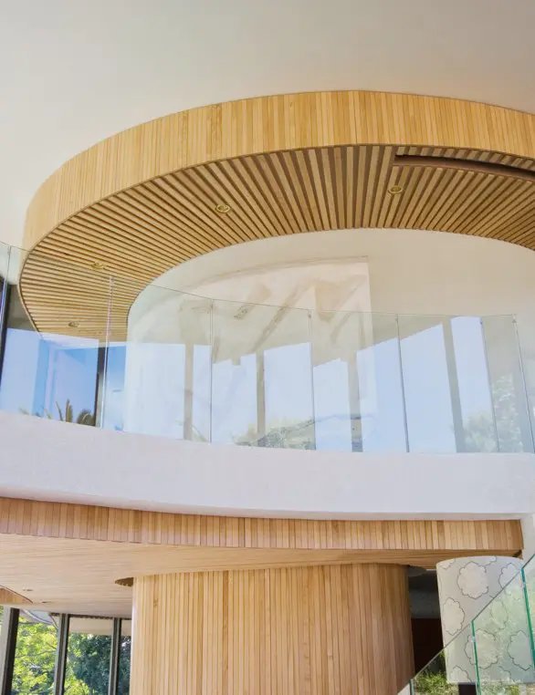 Modern interior with a curved wooden slat ceiling, glass railing, and white walls.