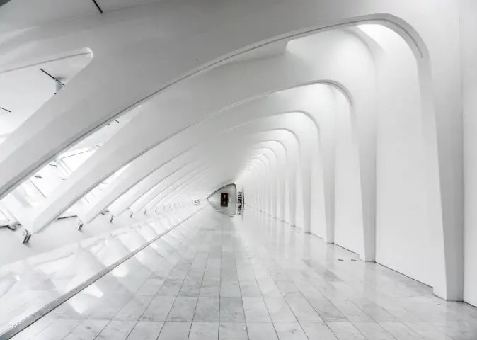 Perspective view of a long, white futuristic corridor with repeating arch structures and reflective tiled flooring.
